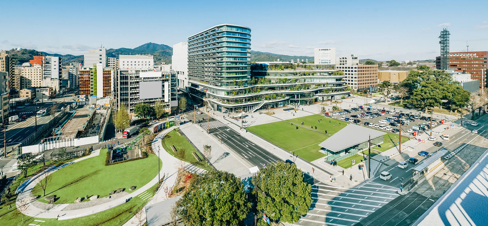くまもと街なか広場（花畑広場）の全景。芝生広場の奥に緑のテラスをもつ建物が見える